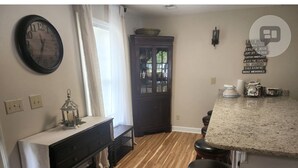 A kitchen with a wooden floor, a dark wooden table with a white tablecloth, a clock, and a cabinet with glass doors. - Beautiful views on Lake Wateree with large screened in porch, 3 bedroom, 2 bath. (Camden)