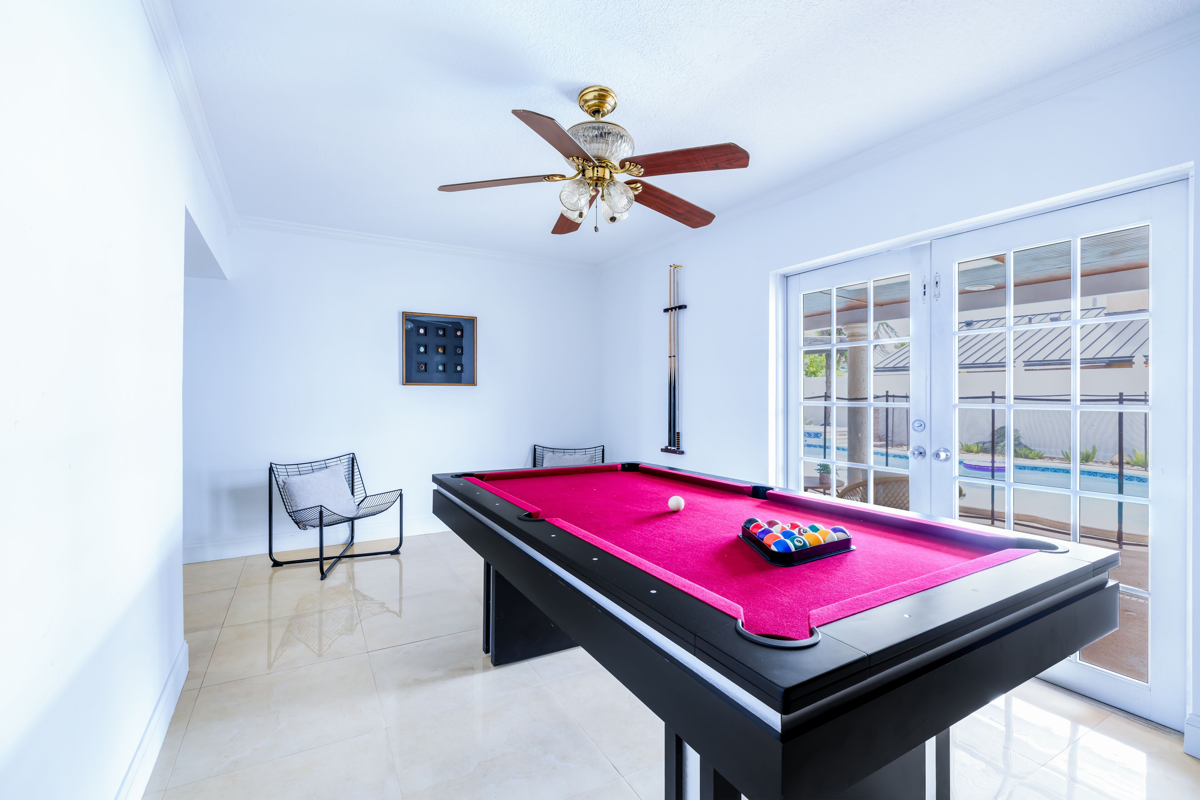 A pool table with a ceiling fan, chairs, and a door leading to an outdoor area.