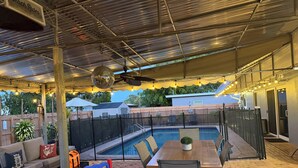 Un patio al aire libre con piscina, mobiliario y una zona cubierta.