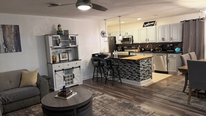 Una cocina moderna con armarios blancos, una isla central y un área de comedor con sofá gris y mesa de centro redonda.