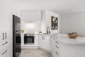 A modern kitchen with white cabinetry, stainless steel appliances, and a white countertop. - Elevated Mount Location, Beach, Shops, 2 Car Parks (Mount Maunganui)