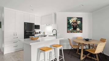 A modern kitchen with white cabinetry, a black refrigerator, and a wooden island with stools.