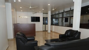 Eine Lobby mit einer Rezeption, schwarzen Ledersofas, Deckenventilatoren und einem großen Fenster.