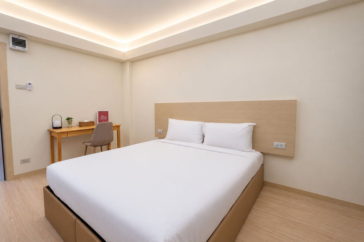Une chambre d’hôtel comprenant un lit, une table de chevet, une chaise, un bureau et un panneau de commande fixé au mur.