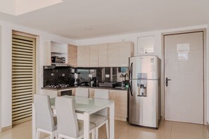 Eine kleine Küche mit Kühlschrank, Herd und Spüle. Ein Esstisch mit Stühlen steht bereit.