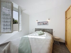 Ein Schlafzimmer mit einem Bett, einem Fenster mit Spitzenvorhängen, einem Nachttisch und einem Bild an der Wand.