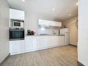 Eine moderne Küche mit weißen Schränken, einer Mikrowelle, einem Backofen, einer Kaffeemaschine und einem Kühlschrank.
