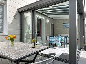 Ein moderner Außenbereich mit Sitzgelegenheit, einem Glastisch, Stühlen und einer Weinflasche.