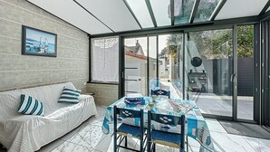 A modern living room with a sofa, a dining table with chairs, and a large glass door leading to a garden. - Ty Ar Mor by Interhome (La Bernerie-en Retz)