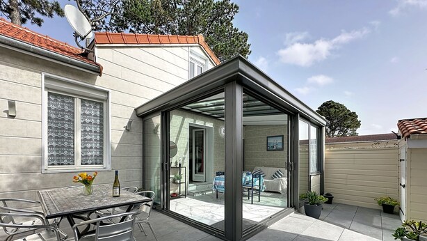 A modern patio with a glass enclosure, a dining table with chairs, and potted plants. - Ty Ar Mor by Interhome (La Bernerie-en Retz)