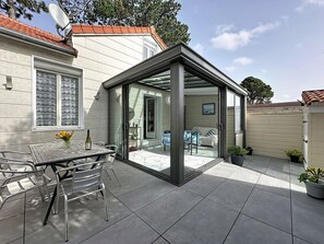 Een moderne patio met glazen wanden, een eettafel met stoelen en potplanten.