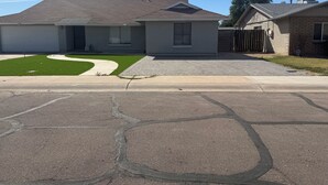 Uma rua residencial com duas casas, uma entrada de automóveis e uma calçada.