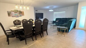 Uma sala de estar espaçosa com uma mesa de jantar e cadeiras, um sofá e uma televisão.
