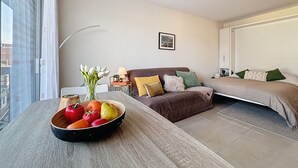Un dormitorio moderno con cama, sofá, una mesa de comedor con fruta y una ventana.