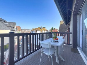 Een balkon met een tafel en stoelen, een vaas met fruit, en uitzicht op de stadsgezicht.