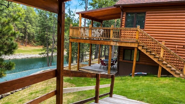A wooden deck with a view of a lake and a cabin. - Beaver Lake Pond & Pines Cabin (Custer)