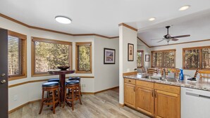 A kitchen with wooden cabinets, a granite countertop, and a dining area with a round table and stools. - Beaver Lake Pond & Pines Cabin (Custer)