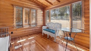 A log cabin interior with wooden walls, a wicker sofa with blue cushions, a glass table, and a chair. - Beaver Lake Pond & Pines Cabin (Custer)