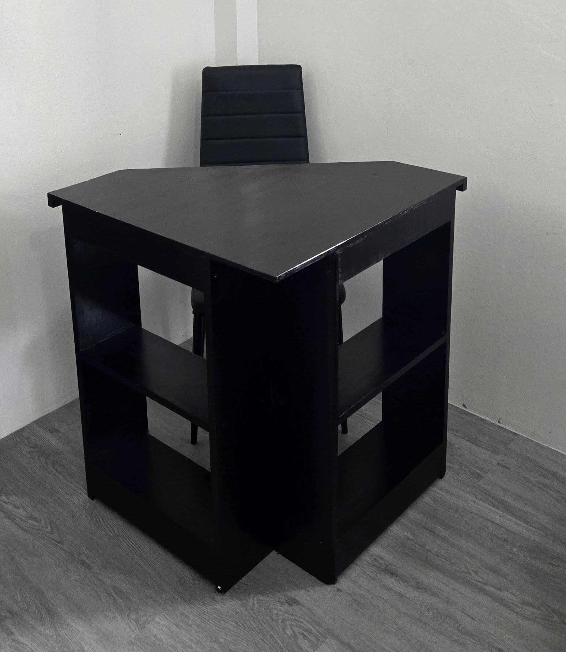 Een zwart hoekbureau met planken, een stoel en een grijze houten vloer.