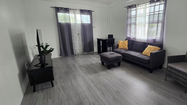 Una sala de estar moderna con un sofá gris, un sillón de mimbre, una mesita y un mueble para la televisión.