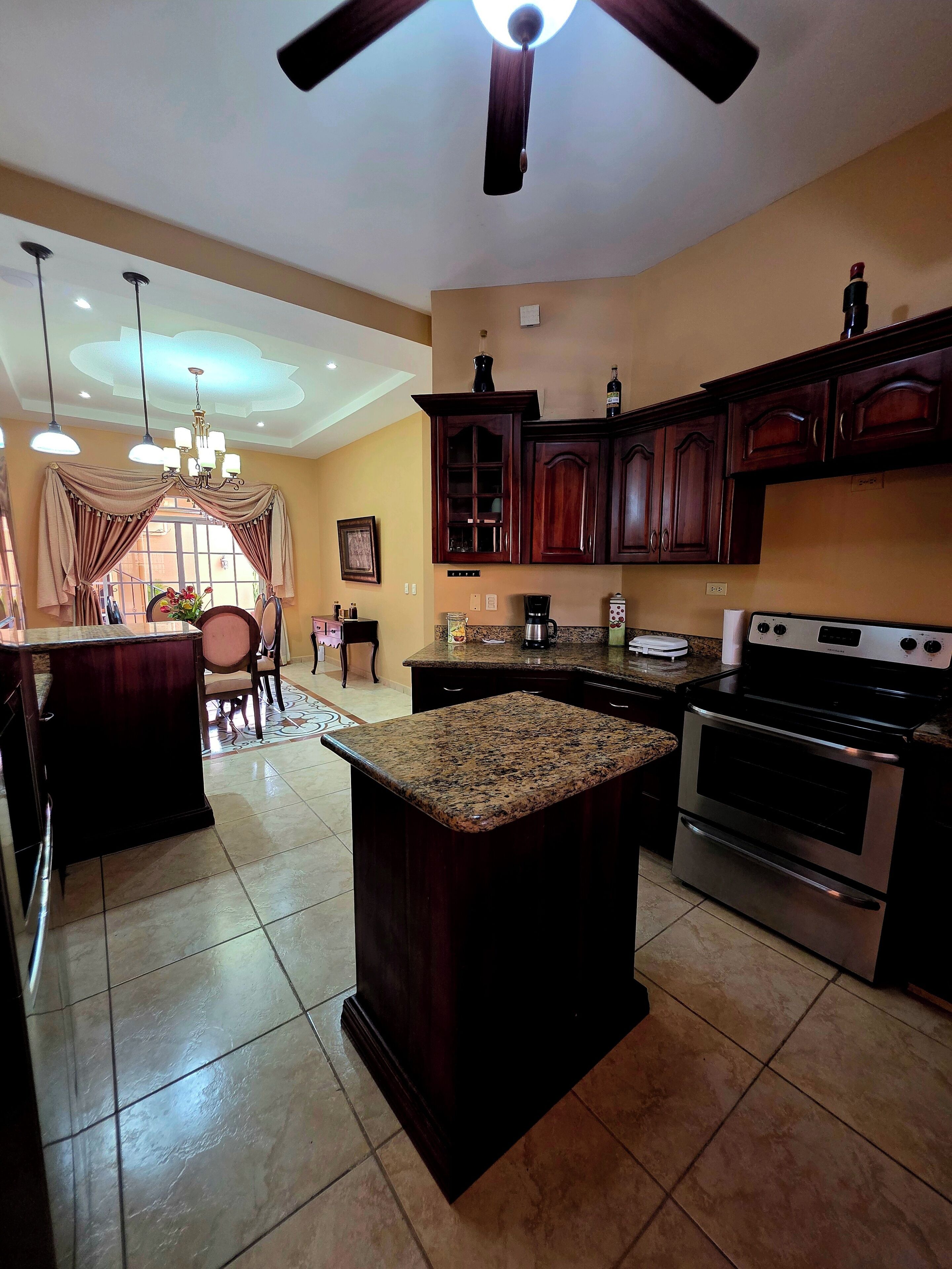 A kitchen with a central island, dark wooden cabinets, a stove, and a ceiling fan.