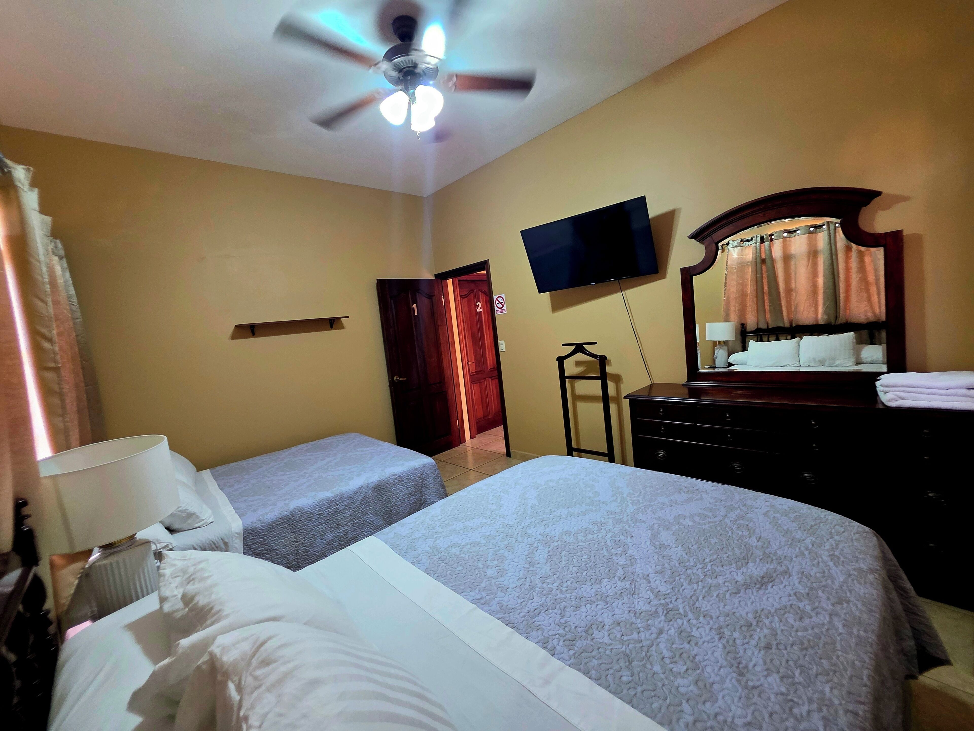 A hotel room with two beds, a ceiling fan, a TV, a dresser, and a mirror.