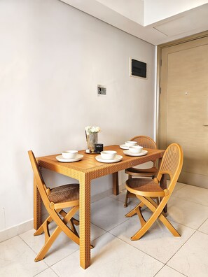 A dining area with a wooden table and chairs, a vase with flowers, and a small black object on the wall. - Teras By SanLiving - 3BR - Hublife Mall (Jakarta)