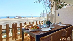 Une table à manger dressée avec des assiettes, des bols de fruits et des tasses, offrant une vue sur la côte.
