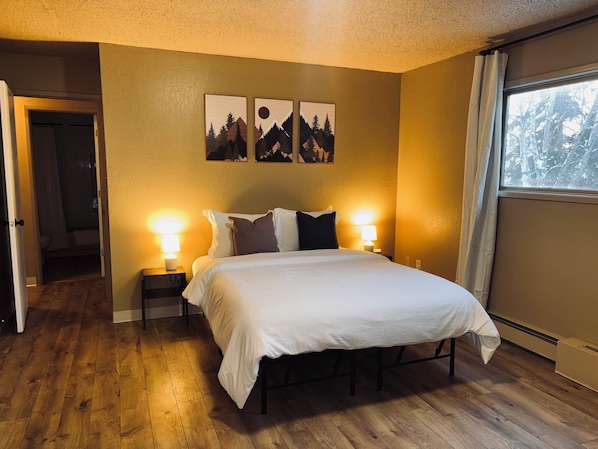 Habitación de hotel con una cama grande, dos lámparas de noche y tres cuadros en la pared que representan montañas y árboles.