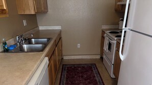 Una cocina compacta con armarios de madera, lavavajillas, refrigerador y pileta.