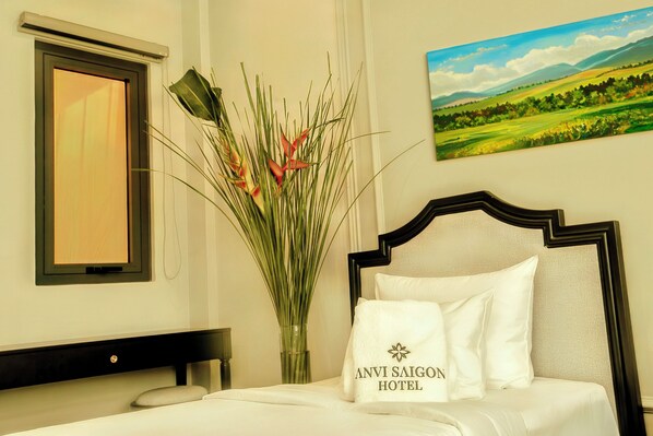 A hotel room with a bed, a vase with flowers, a painting of a landscape, and a sign with the hotel name. - Anvi Saigon Boutique Hotel (Ho Chi Minh City)