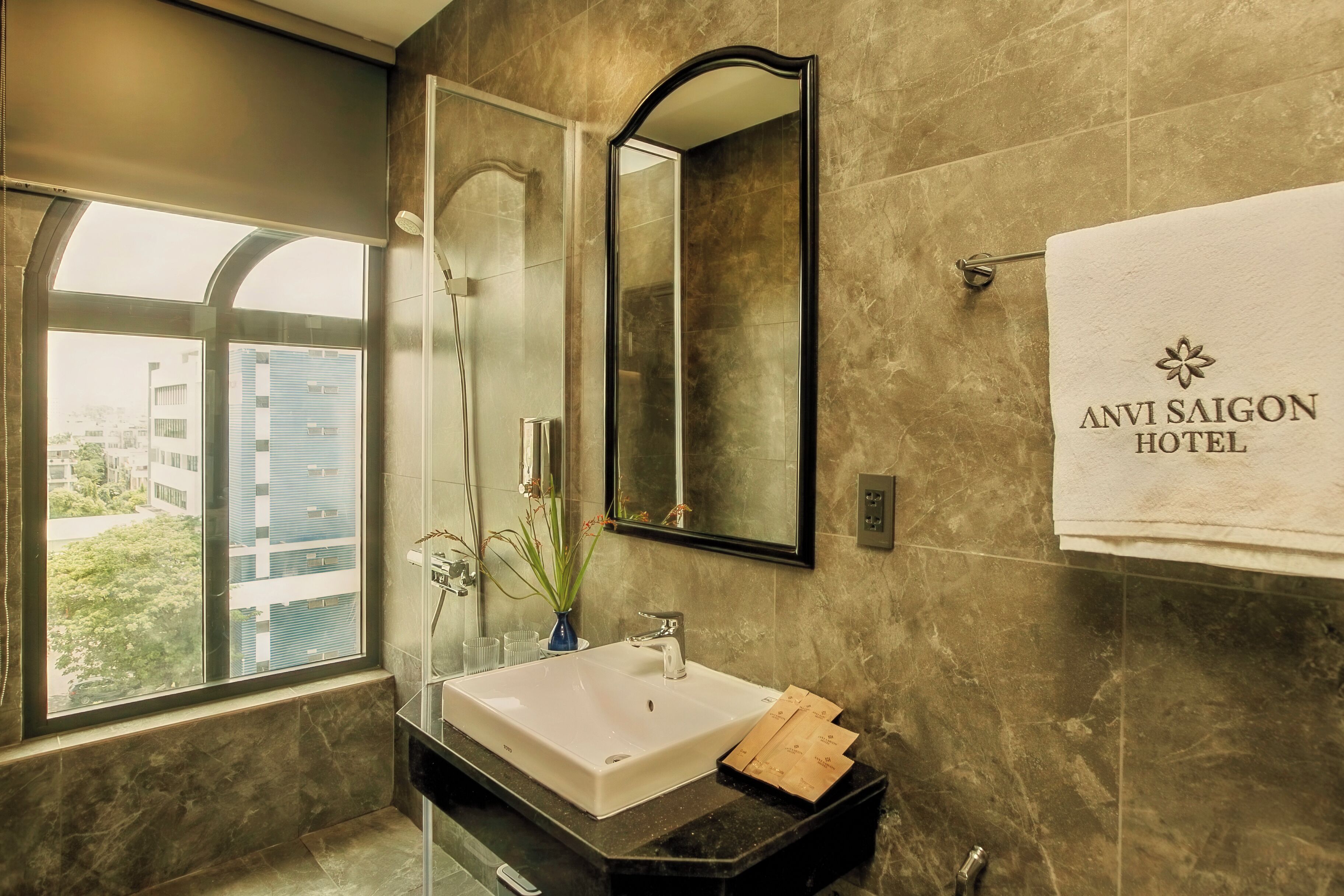 Un bagno moderno con un'ampia finestra, un lavandino, uno specchio e un asciugamano con la scritta 'ANVI SAIGON HOTEL'.
