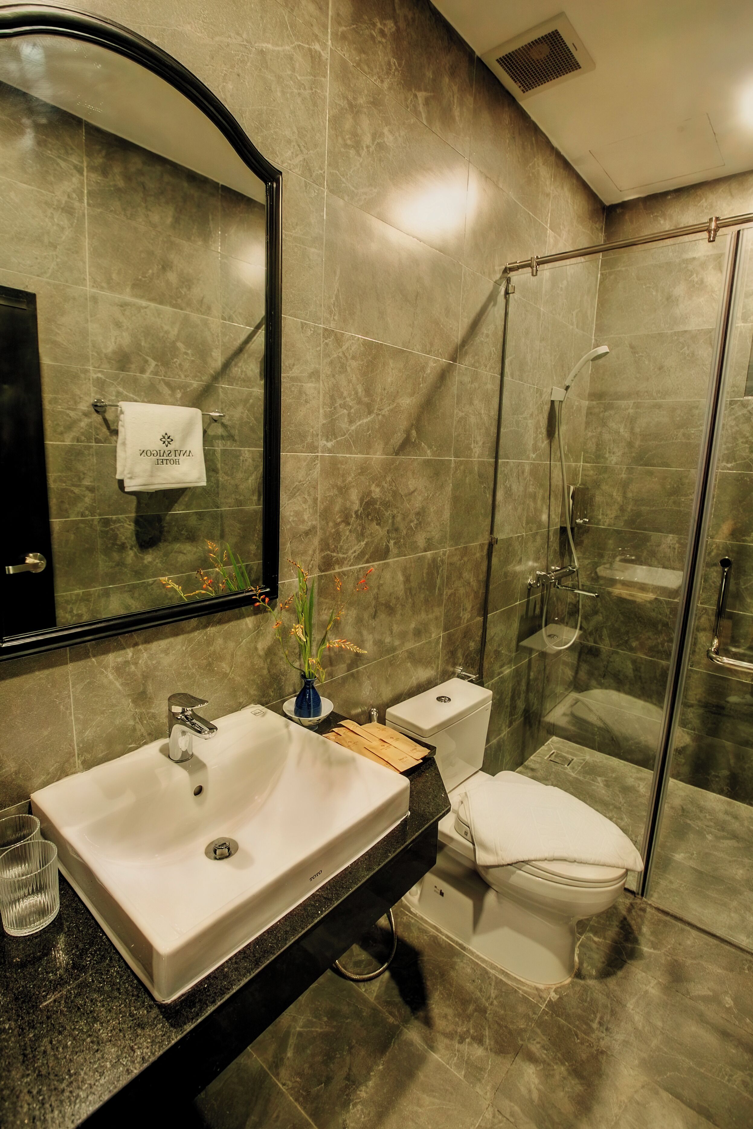 A modern bathroom with a large mirror, a sink, a toilet, and a glass-enclosed shower.