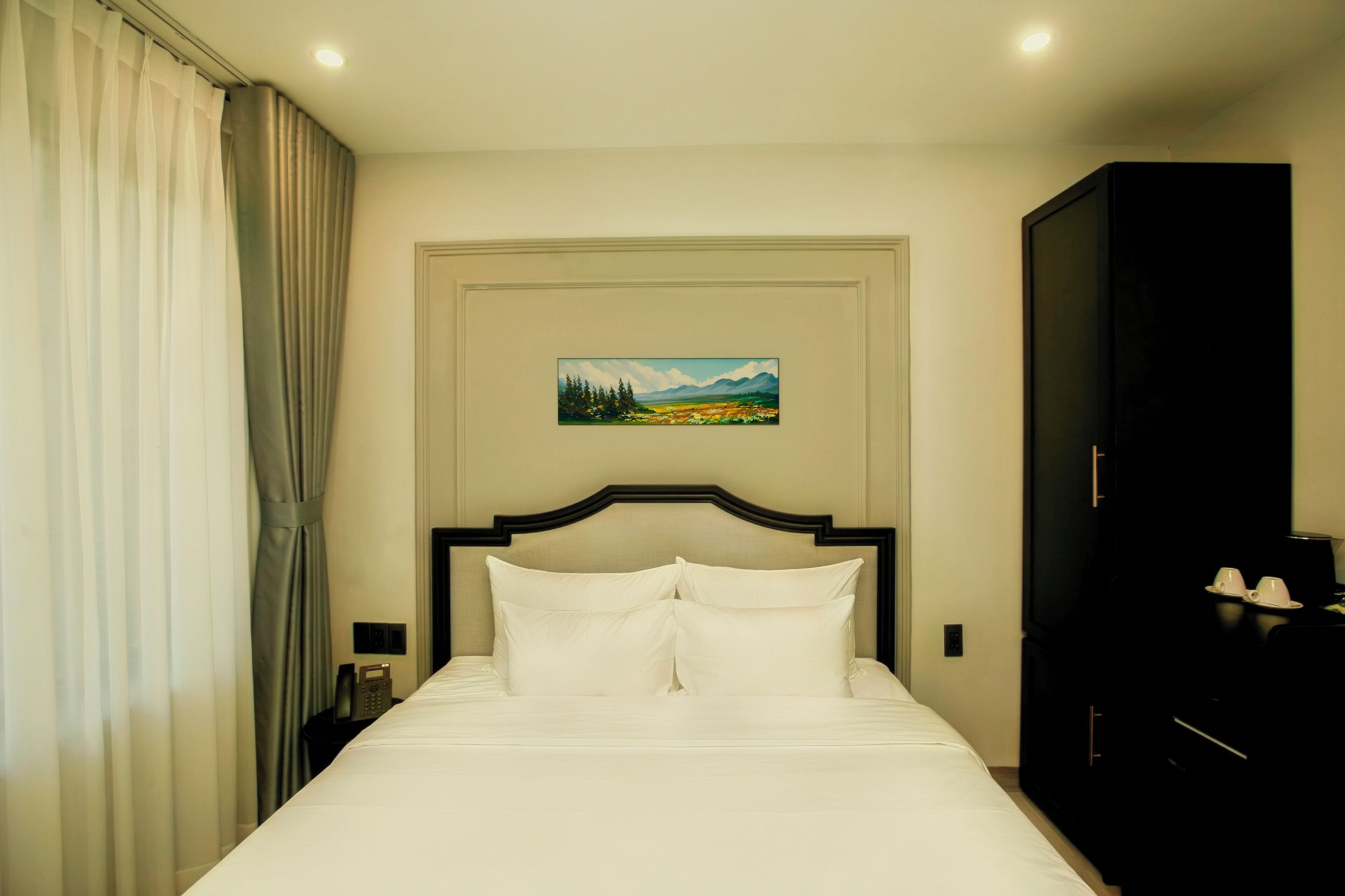 Een hotelkamer met een bed, een schilderij aan de muur, een nachtkastje en een kledingkast.