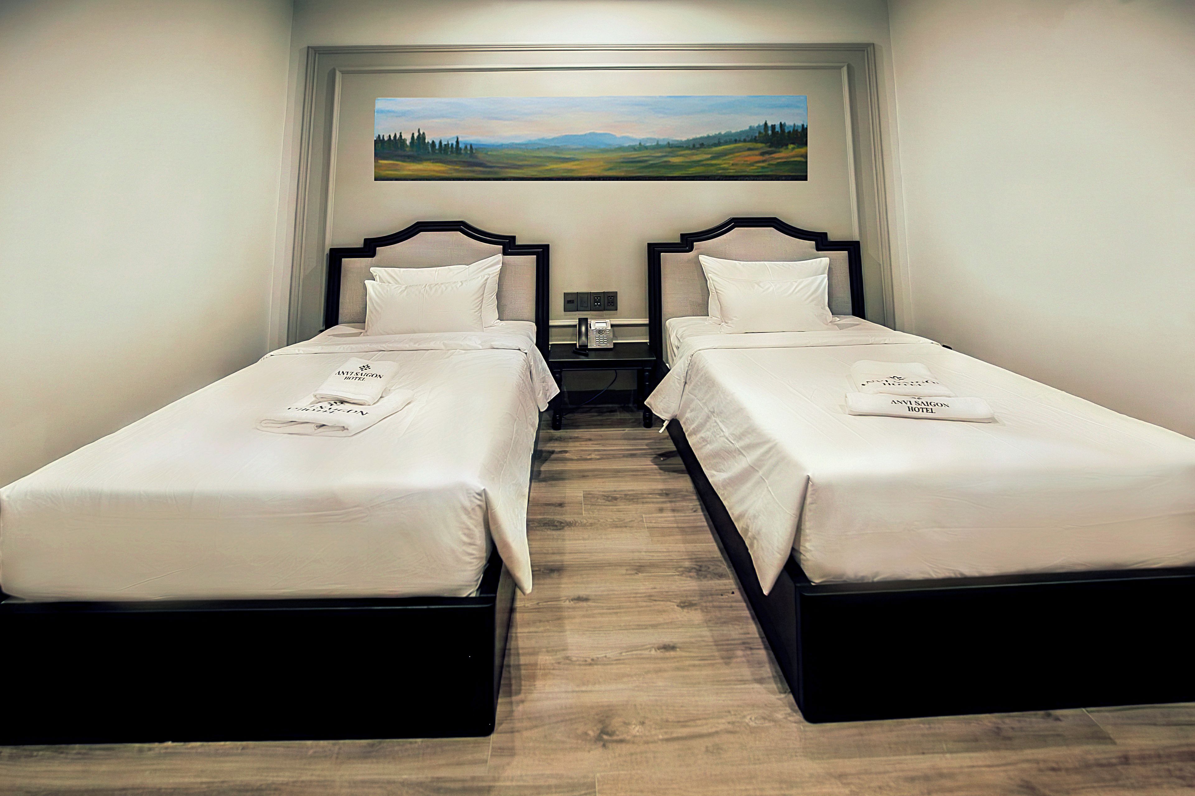 Habitación de hotel con dos camas individuales, un cuadro de un paisaje en la pared y piso de madera.