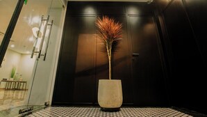 A modern interior with a tall, textured vase with a plant, a dark wooden door, and a tiled floor. - Anvi Saigon Boutique Hotel (Ho Chi Minh City)