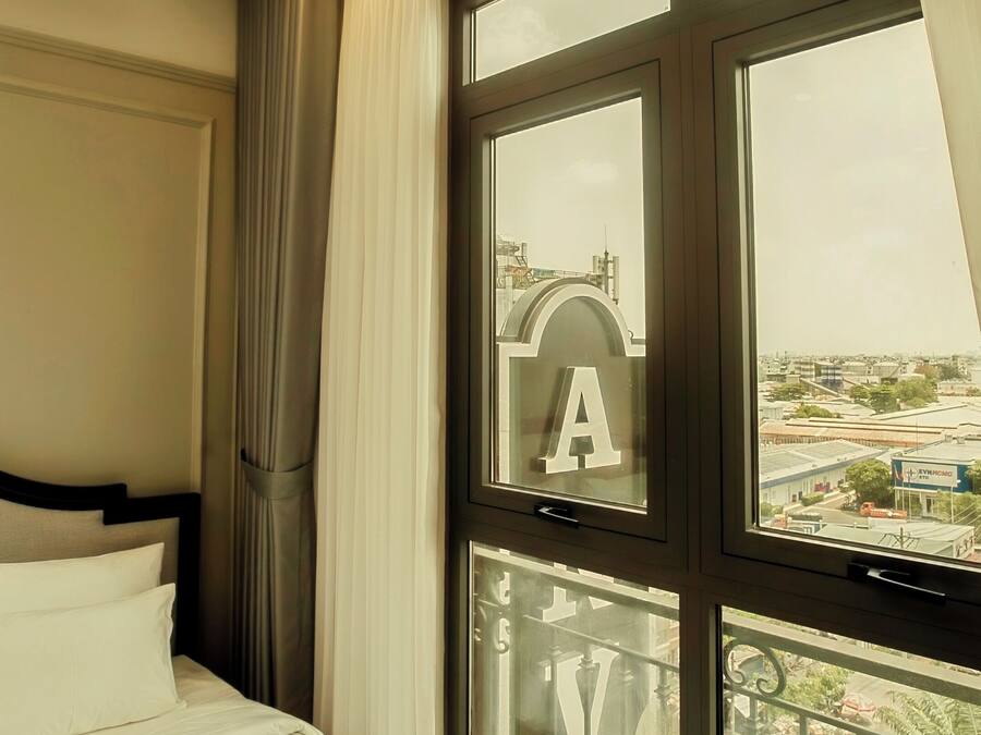 Une chambre d’hôtel avec un lit, une grande fenêtre avec des rideaux et un balcon doté d’une balustrade.