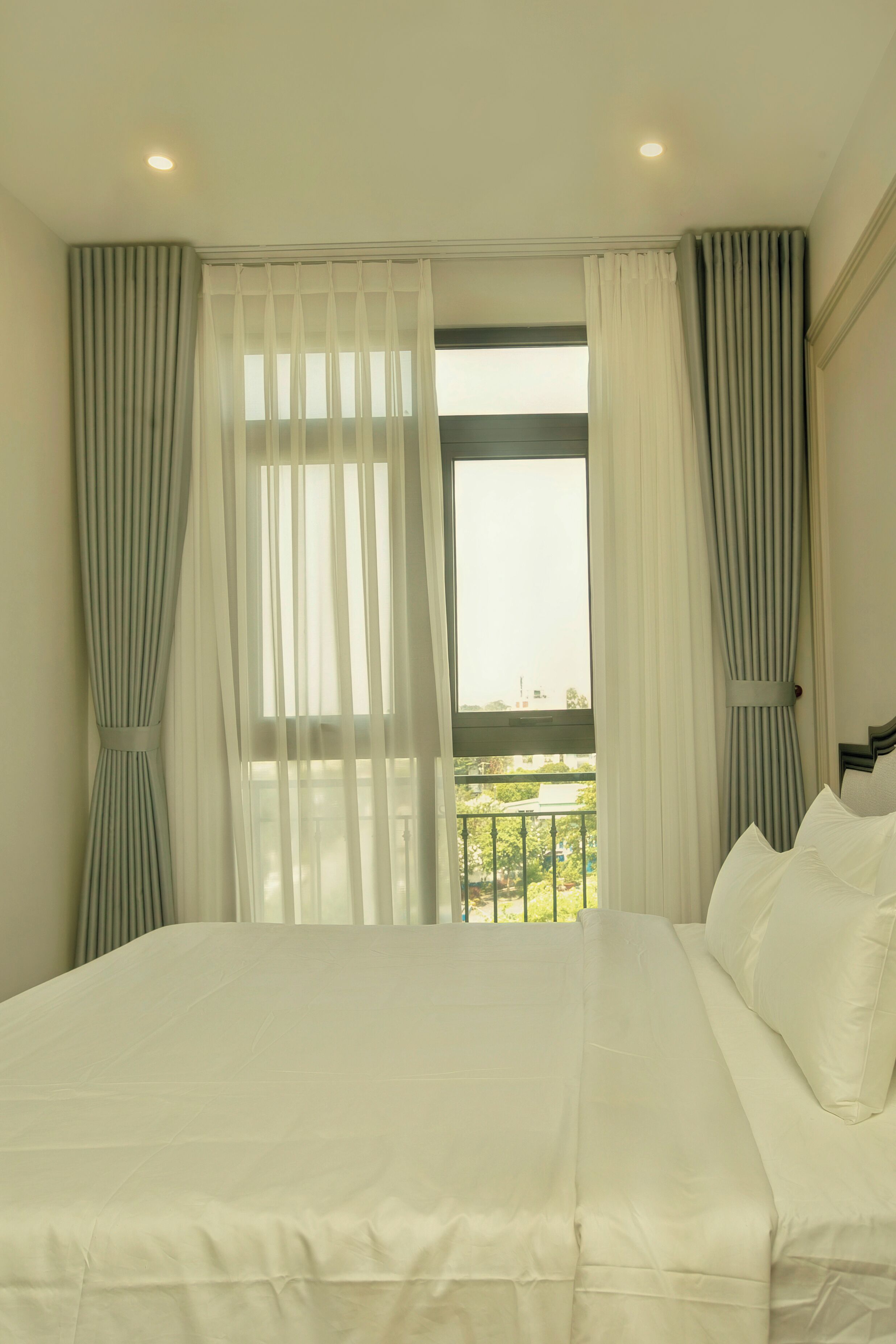 A hotel room with a bed, curtains, a window with a view, and a balcony.