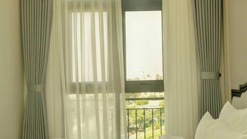 A hotel room with a bed, curtains, a window with a view, and a balcony.