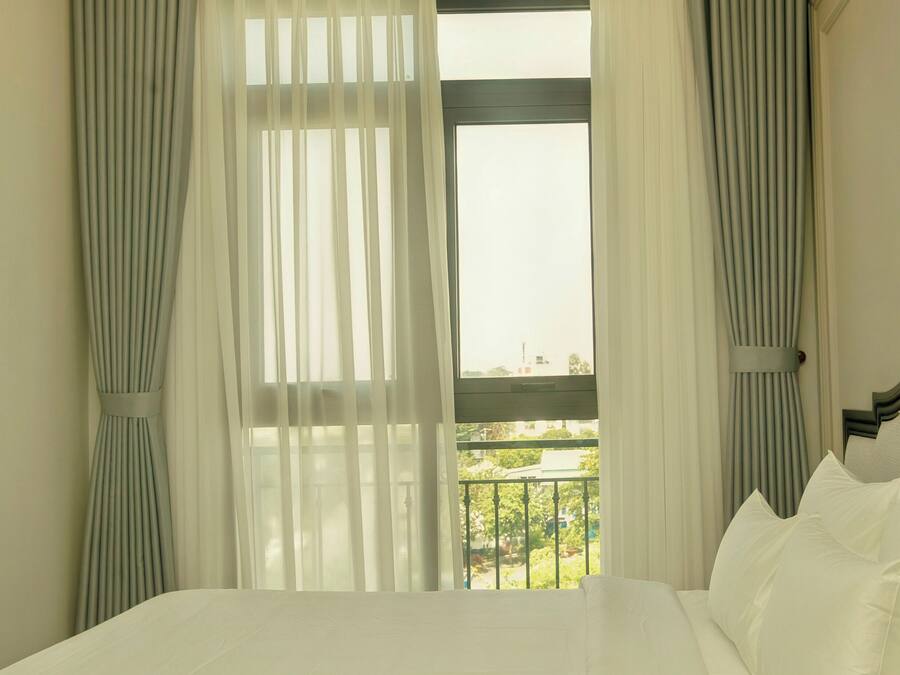 A hotel room with a bed, curtains, a window with a view, and a balcony.