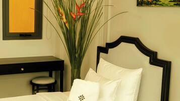 A hotel room with a bed, a desk, a vase with plants, and a painting on the wall.