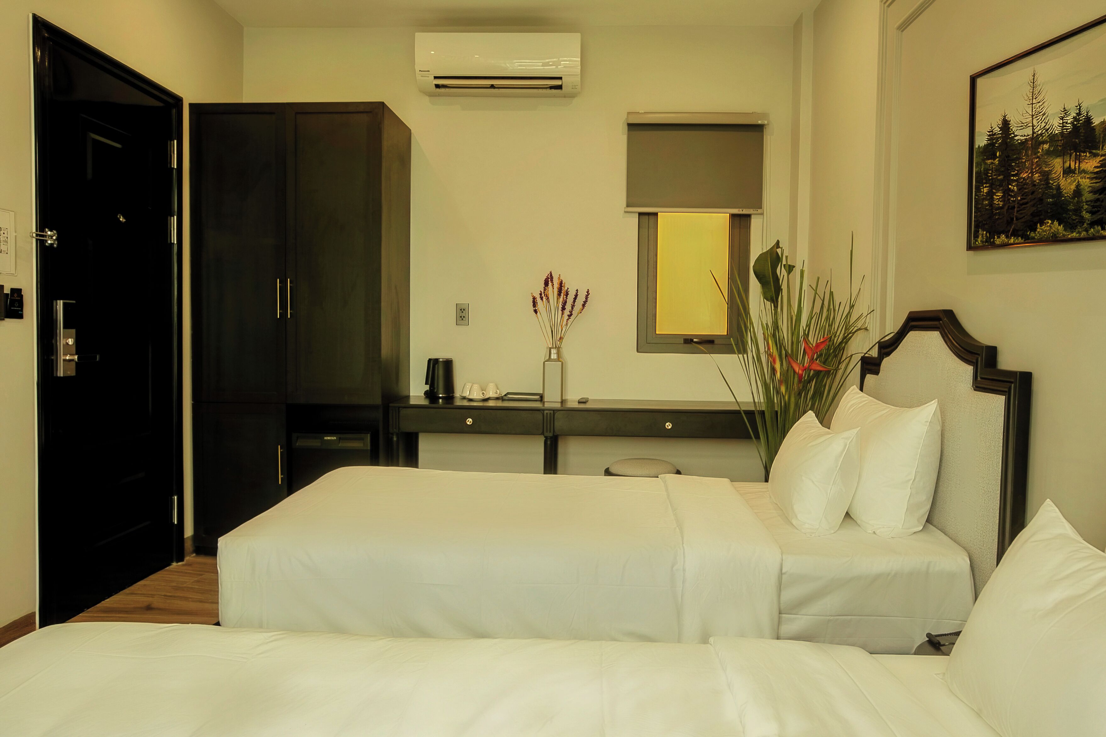 A hotel room with two beds, a desk, a mirror, and an air conditioning unit.