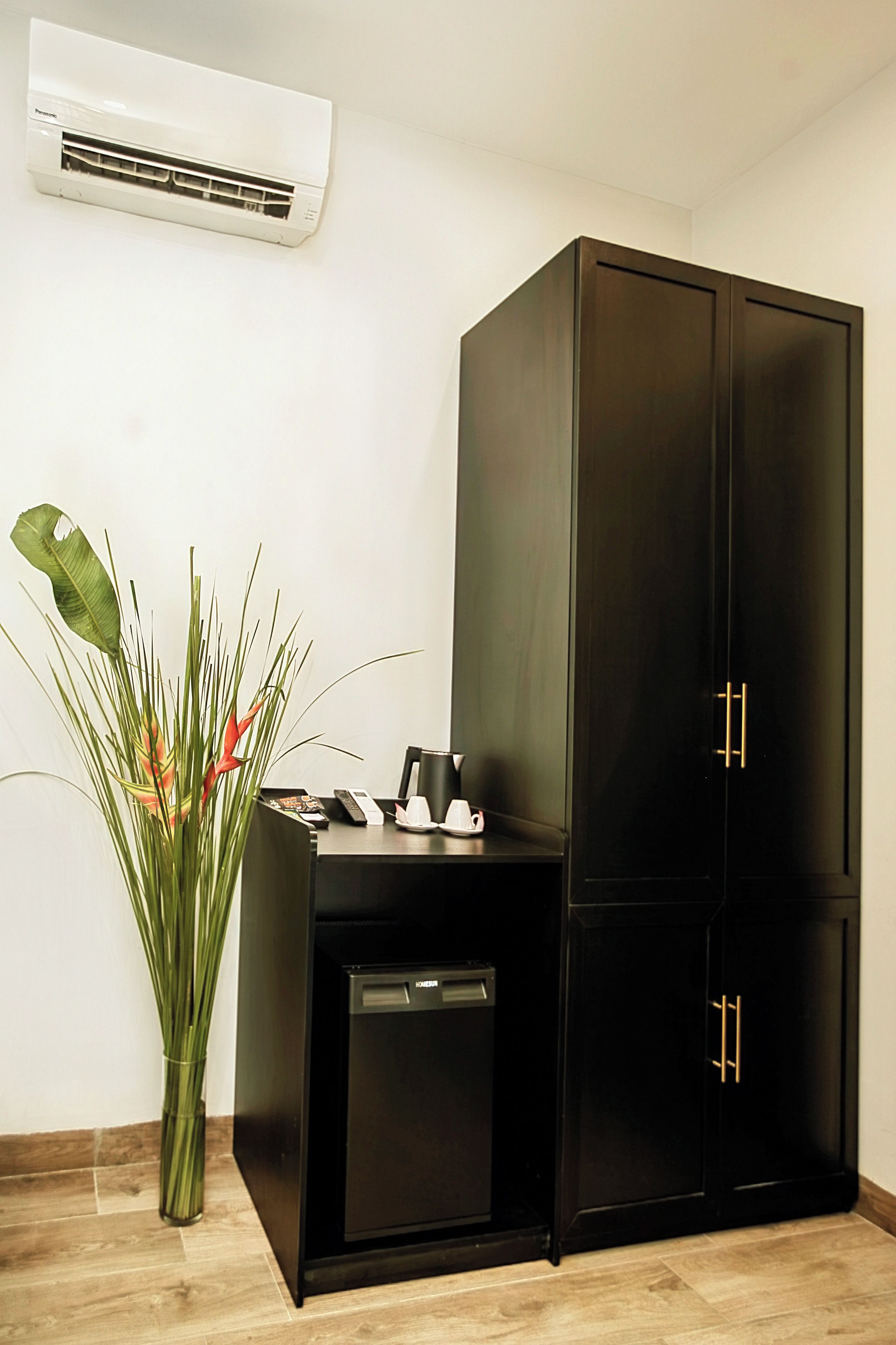 A black cabinet with two doors, a small black cabinet with a coffee maker, and a plant with green leaves and red flowers.