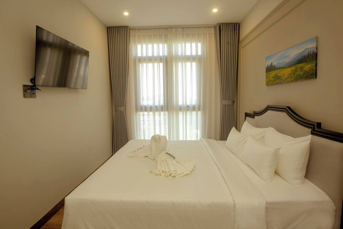 A hotel room with a bed, a flat-screen TV, a painting, and a window with curtains.