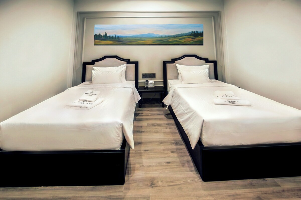 Ein Hotelzimmer mit zwei Einzelbetten, einem Landschaftsbild und einem Holzboden.