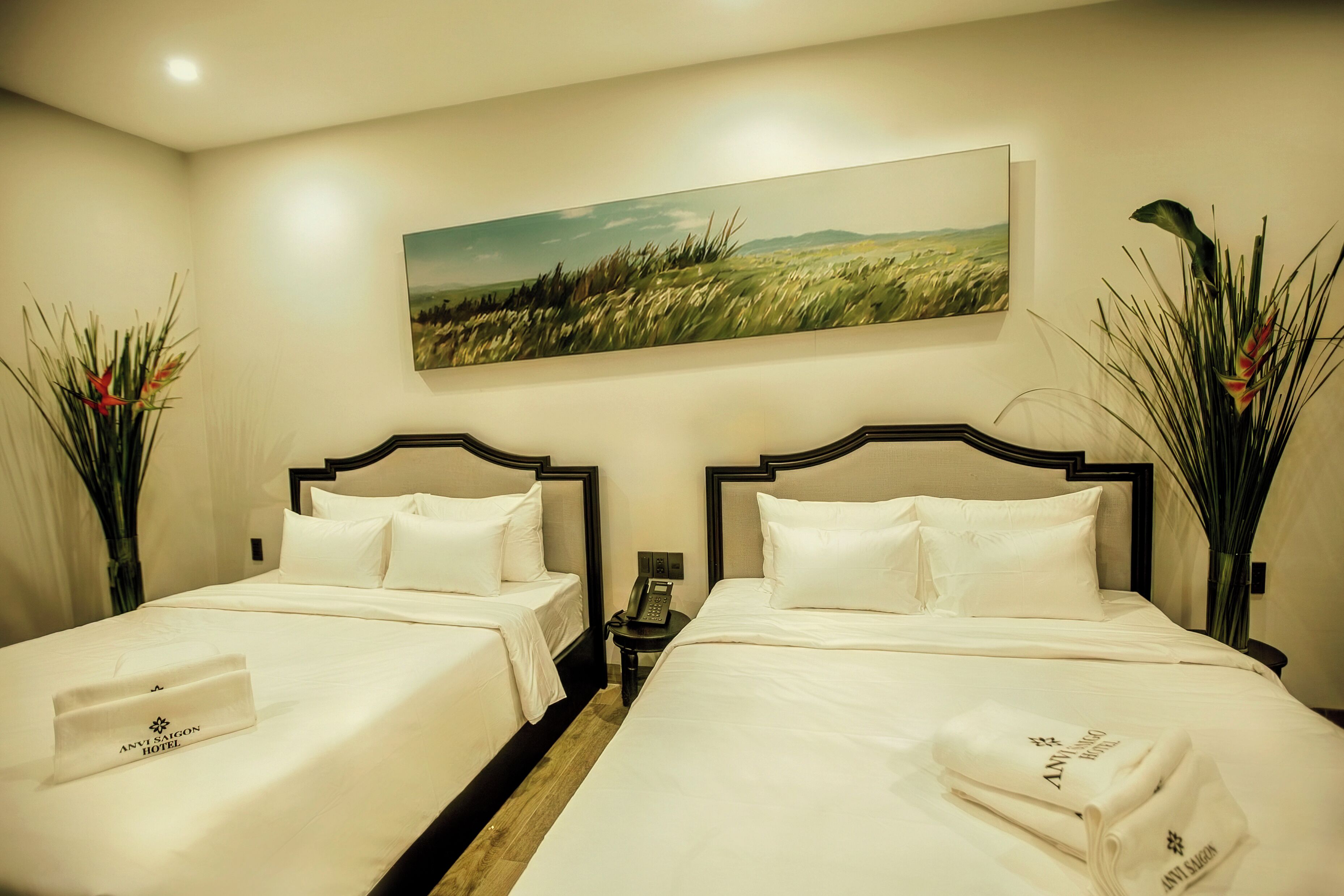 A hotel room with two beds, a painting on the wall, and a nightstand with a phone.