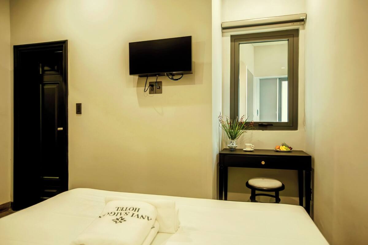 A hotel room with a bed, a TV mounted on the wall, a small desk with a chair, and a mirror above the desk.