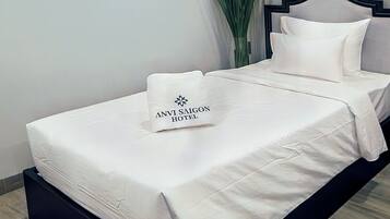 Ein ordentlich bezogenes Bett mit einem Kopfkissen, auf dem 'ANVI SAIGON HOTEL' steht, und ein Landschaftsbild an der Wand.