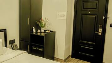 A hotel room with a bed, a wardrobe, a desk with a plant, and an air conditioning unit.