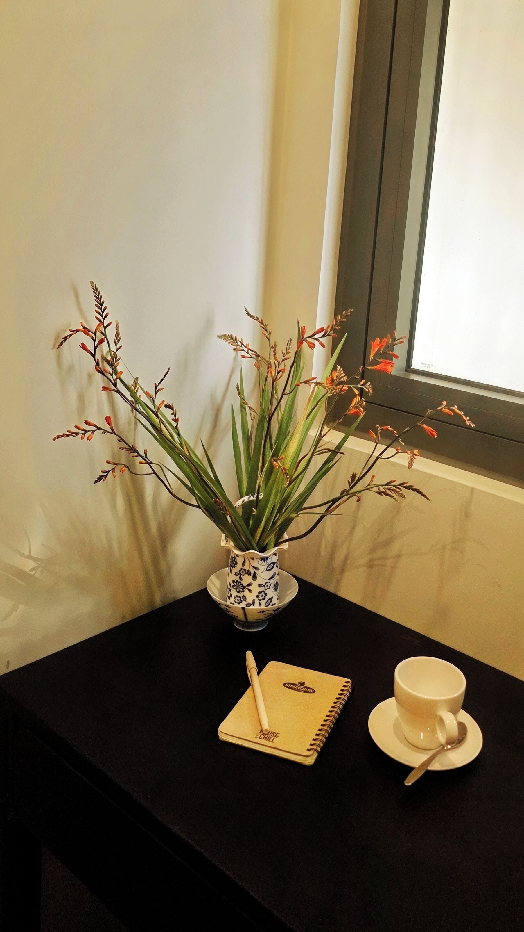A table with a vase of flowers, a notebook, and a cup.